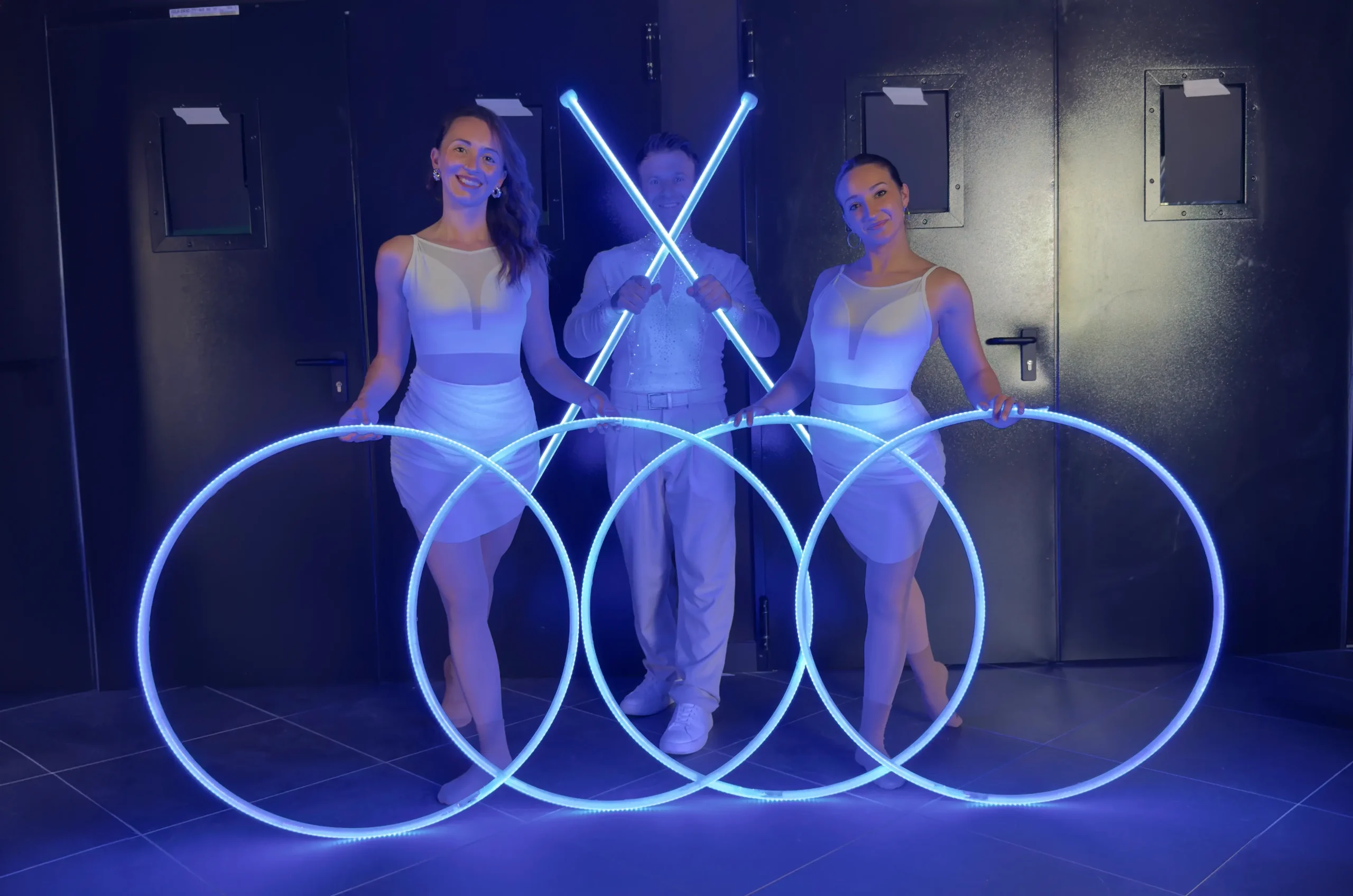 Gruppo di tre performer con costumi bianchi e attrezzi scenografici a LED azzurri con cerchi e bastoni luminosi per uno show di car reveal.